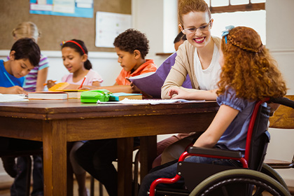 Photo d'un enfant en classe en fauteuil roulant avec une éducatrice spécialisée